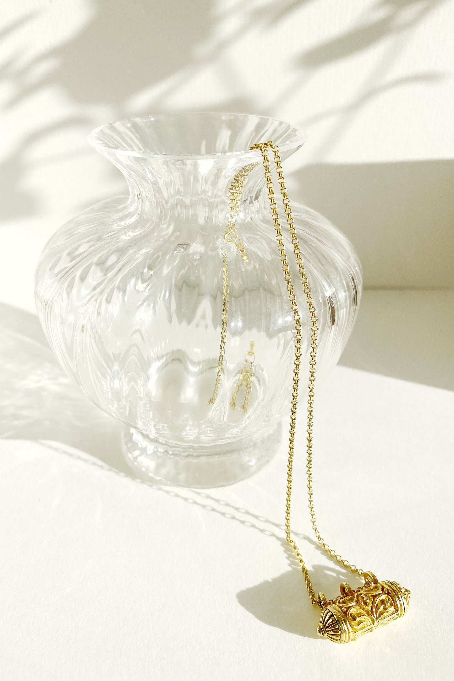 Kiaria Wishing Locket with chain draped over rim of glass vase