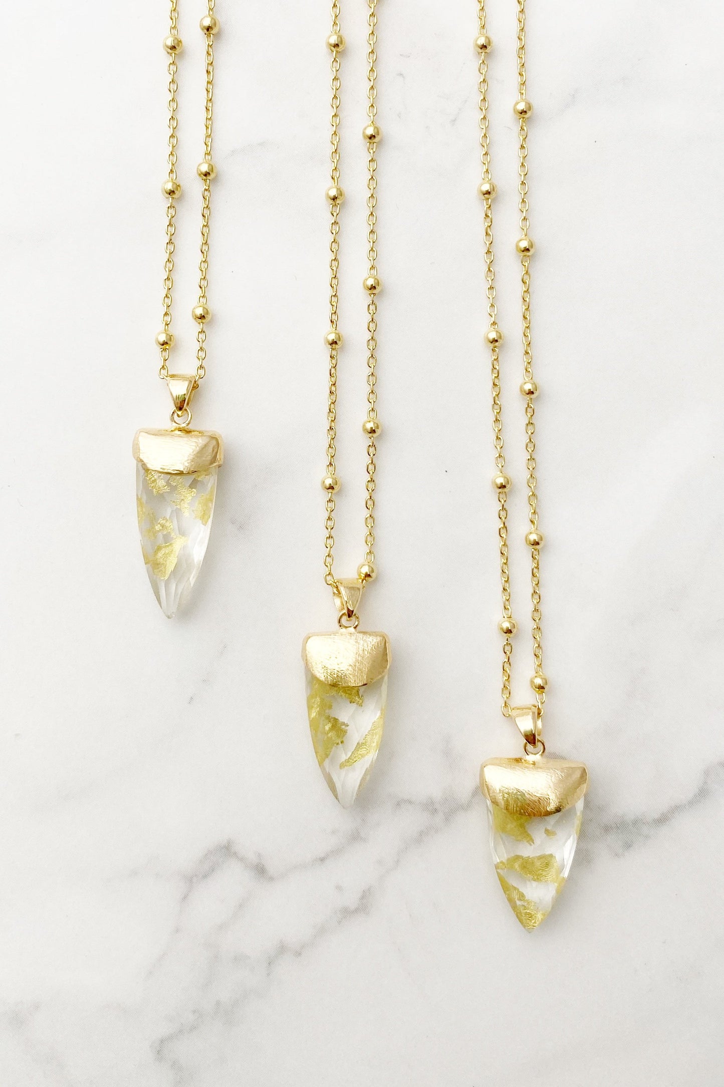 Three Guardian Clear Quartz Shield necklaces on a surface